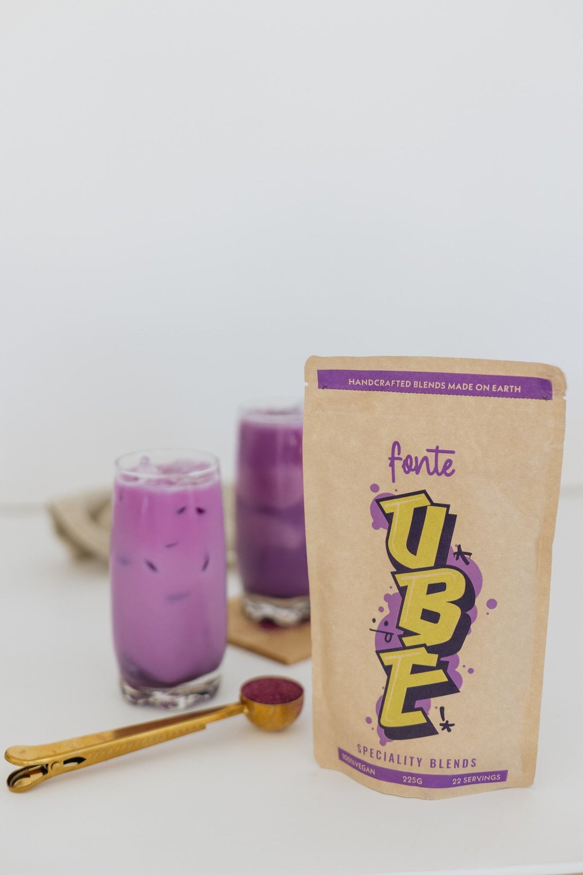 Ube Latte servido frío en vaso con hielo, junto al paquete de FONTE de 225 gr.